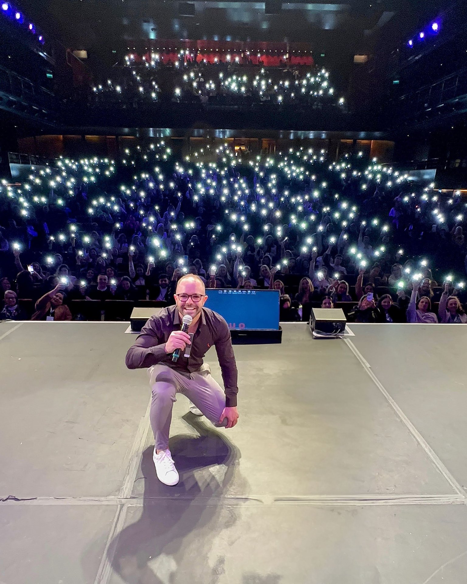 Rick Fernandes no palco durante uma palestra para plateia lotada